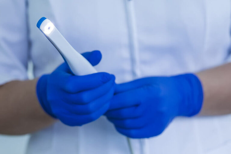 Doctor with gloved hands holding an intraoral camera that is used to scan digital impressions of the mouth.